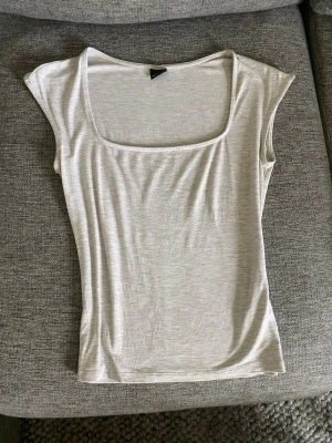 Ljusgrå topp - Snygg ljusgrå topp ifrån Gina Tricot med ribbad struktur och fyrkantig ringning. Toppen är kortärmad och har en tight passform som framhäver figuren. Perfekt att styla med jeans eller kjol för en clean look.