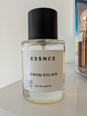 ESSNCE Lemon Eclair Eau de Parfum - Fräsch parfym från ESSNCE med doft av Lemon Eclair. Flaskan är rund och genomskinlig med svart lock och vit etikett. Innehållet är ljusgult och flaskan har en stilren, minimalistisk design. Perfekt för dig som gillar citrusdofter. Jag säljer den för samma pris som jag köpte den för. Använd lite. 