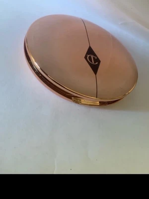 Charlotte Tilbury puderfoundation Setting powder Medium - Säljer en puderfoundation från Charlotte Tilbury i en snygg roséguldig oval dosa med spegel. Färgen är ljusbeige och formulan är pressat puder. Perfekt för en naturlig och jämn bas. Dosan har märkets logga på locket.