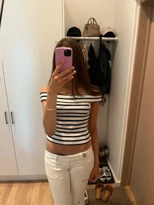 Randig offshoulder topp - Säljer en vit och svart randig offshoulder topp med croppad passform. Toppen är ribbad och har en snygg båtringad design som sitter precis ovanför axlarna. Perfekt för dig som vill ha en trendig och bekväm topp till sommaren. skrov om ni har frågor💗Använd 3-4 gånger