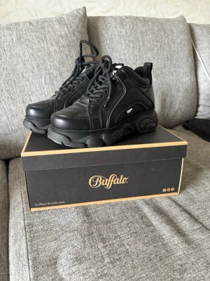 Buffalo svarta chunky sneakers - Buffalo sneakers i helsvart med chunky sula och klassisk snörning. Skorna har en högre plattformssula och är tillverkade i syntetläder med detaljerade sömmar och logga på sidan i storlek 38 men passar 39. De är endast använda fåtal gånger och förutom lite lort är de i perfekt skick. Nypris: 789kr. 