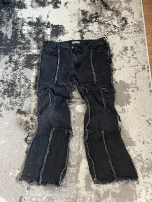 Svarta patchwork jeans med råa kanter - Unika svarta jeans med patchwork-design och råa, fransiga sömmar över hela byxan. Modellen har raka ben och klassisk femficksdesign. Perfekta för dig som gillar en edgy och trendig streetstyle-look. Bought for 160€