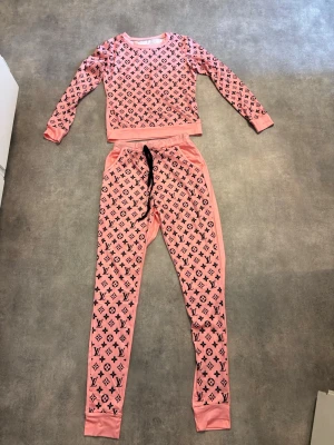 Mönstrad rosa tröja med byxor/leggings till. - 2-delad dress med tröja och byxor/leggings till. Mönster på ena sidan av tröjan och byxorna, enfärgat på andra sidan. Väldigt mjukt. Fickor på sidorna och snörning i midjan. Setet är helt nytt och köpt i storlek S