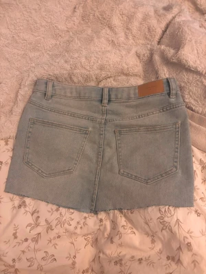 Ljusblå jeanskjol med rå kant - Trendig ljusblå jeanskjol i kort modell. Perfekt till vardags för en avslappnad och cool look.