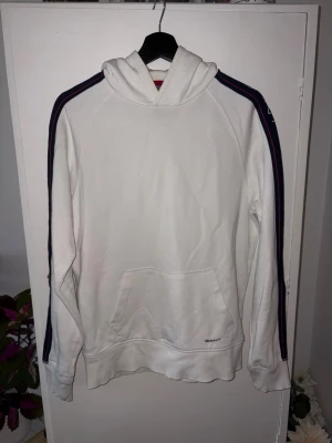Gant Hoodie M - Säljer denna snygga Gant hoodie med blå rand längst ärmarna. Storlek M. Rensar garderoben och säljer pga för lite användning.