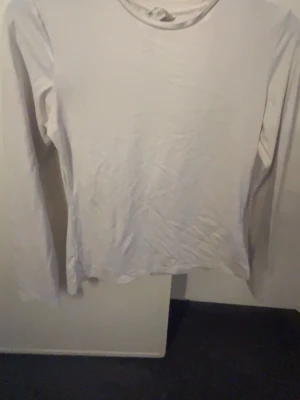 Vit långärmad topp i bomull - En basic vit långärmad topp i mjuk bomull. Enkel och stilren design med rund halsringning, perfekt att matcha med olika outfits. Passar dig som gillar en clean och klassisk look.