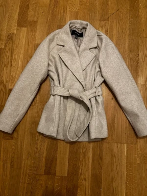 Beige kappa från Vero Moda - Stilren beige kappa från Vero Moda med knytskärp i midjan och breda slag. Kappan har en klassisk, rak passform. Perfekt för dig som vill ha en enkel men trendig look. tveka inte att höra av dig, om du har frågor 💖