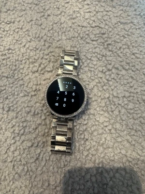 Silver smartklocka från Michael kors - Snygg martklocka i silver med rund urtavla och stålarmband. Klockan har en ram dekorerad med små stenar som ger extra bling. Pekskärm med digital display och flera funktioner. Perfekt accessoar för dig som gillar teknik och stil.
