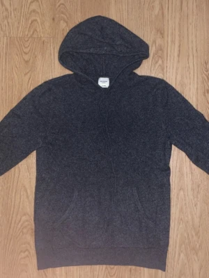 Mörkgrå cashmere hoodie John Henric - Mysig mörkgrå hoodie från John Henric i lyxig cashmere. Klassisk modell med huva och dragsko, samt magficka framtill. Perfekt för dig som vill ha en stilren och bekväm hoodie i ett riktigt mjukt material.