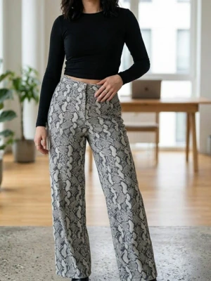 Vida byxor med ormmönster - Säljer ett par vida byxor med grått och svart ormmönster. Byxorna har hög midja och raka ben, vilket ger en trendig och avslappnad look. Materialet är mjukt och stretchigt för extra komfort. Perfekta för dig som vill sticka ut med ett coolt mönster.