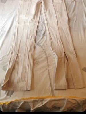 Beige leggings med slits framtill - Säljer ett par beige leggings med trendiga slitsar framtill vid bensluten. De har en smal passform och är tillverkade i ett stretchigt material som sitter snyggt på benen. Perfekta för dig som gillar en stilren och modern look.