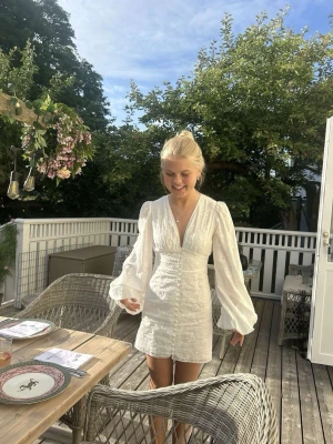 ADOORE liknande vit  kortklänning till student/midsommar - Superfin vit kortklänning lik ADOORE klänningarna från Gina Tricot med broderade blommor, v-ringning och långa puffärmar. Helt ny med lappar.  Klänningen har knappar framtill och markerad midja som ger en snygg siluett. Perfekt för midsommar, student eller annan sommarfest