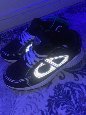 Svarta sneakers med reflekterande detaljer - Säljer ett par svarta sneakers från GAP med vita reflekterande detaljer och vita skosnören. Skorna har en chunky sula i vitt och en sportig design som sticker ut i mörkret tack vare de reflekterande partierna. Perfekta för dig som gillar streetwear.