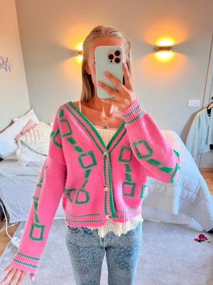 Rosa kofta med grönt mönster - Säljer en superfin rosa kofta med gröna mönster och vita knappar. Koftan har v-ringning, ribbade muddar och avslappnad passform. Perfekt för dig som vill sticka ut lite extra! Passar till jeans eller kjol.