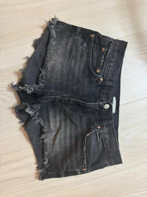 Svarta jeansshorts med fransar - Säljer ett par svarta jeansshorts med slitna kanter och fransar. Shortsen har fem fickor och en cool tvättad look. Perfekta för sommaren och ger en avslappnad vibe.