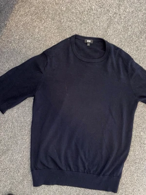 Mörkblå stickad tröja från Uniqlo - En stilren mörkblå stickad tröja från Uniqlo med rund halsringning och ribbade muddar. Tröjan har en klassisk passform och är tillverkad i ett mjukt, tunt stickat material som passar perfekt till lager på lager.