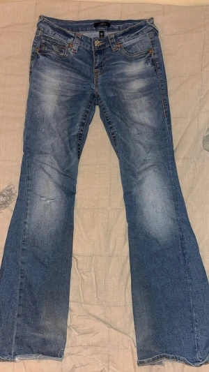 Blå bootcut low waist jeans från True Religion - Säljer dessa true religion jeans för att dom är för stora, jeansen är ganska söndriga där nere. dom hsr också ett litet hål på ena benet.