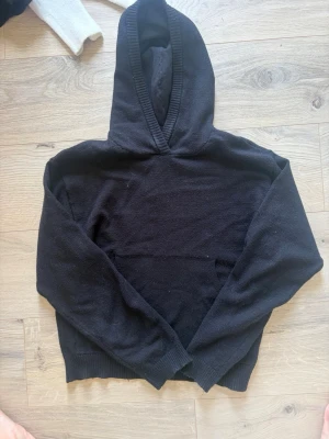 Svart stickad hoodie från bikbok  - Mysig svart hoodie från bikbok i storlek XS. Hoodien har en klassisk huva och ribbade muddar vid ärmslut och nederkant. Perfekt för dig som gillar en enkel och stilren look. Materialet känns mjukt och bekvämt mot huden.