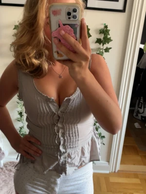 Beige linnetopp med knappar och snörning - Säljer en beige linnetopp från H&M med knappar framtill och snörning på sidorna. Toppen har volangkant nedtill och är ärmlös med en lätt rynkad struktur. Perfekt för dig som gillar en feminin och avslappnad stil.