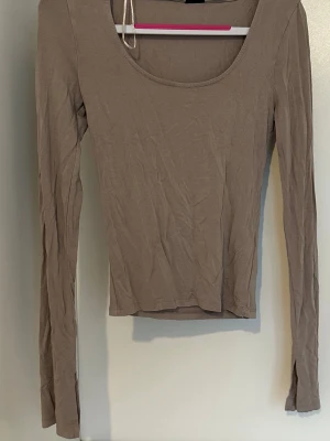 Beige långärmad topp med slits - Snygg beige långärmad topp med rundad urringning och slits vid ärmsluten. Tillverkad i mjukt bomullsmaterial som sitter skönt mot kroppen. Perfekt att styla med jeans eller kjol för en clean look.