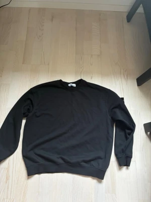 Svart sweatshirt från Stone Island - Säljer en svart sweatshirt från Stone Island med klassisk rund hals och ribbade muddar vid ärmslut och nederkant. Tröjan har en clean look utan tryck eller mönster.
