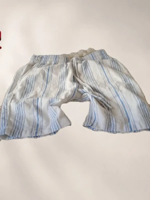 Randiga shorts i bomull - Mysiga shorts med blå och vita ränder. De har resår i midjan för extra komfort och är tillverkade i ett lätt bomullstyg som känns svalt mot huden. Perfekta för lata dagar hemma eller sommarens varma nätter.