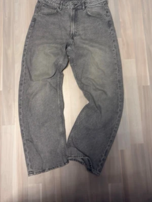 Grå baggy jeans med tvättad look - Säljer ett par grå jeans med baggy passform och tvättad look. Jeansen har klassiska fem fickor och raka ben. Materialet är denim och färgen är en cool grå nyans med lite slitningar på låren. Perfekt för dig som gillar en avslappnad stil.
