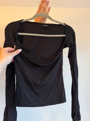 Svart långärmad topp med vid urringning - En svart långärmad topp med vid och figursydd passform. Perfekt att styla med jeans eller kjol.