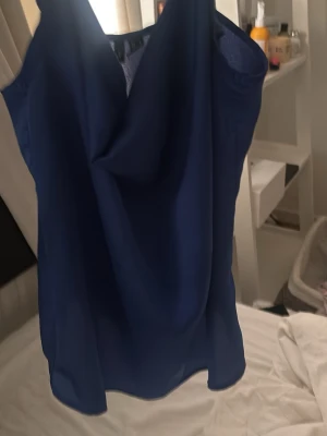 Blå linnetopp med draperad hals - Snygg blå linnetopp med tunna axelband och draperad halsringning. Toppen har en lös passform och är tillverkad i ett lätt, flowy material som känns skönt mot huden. Perfekt att styla med jeans eller kjol för en trendig look.