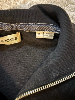 Svart ziptröja från Jack & Jones - Snygg svart ziptröja från Jack & Jones med hög krage och dragkedja framtill. Tröjan har en enkel och stilren design, perfekt att slänga på sig över en t-shirt. Tillverkad i mjukt material för skön känsla.