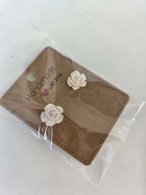 Handgjorda örhängen i form av rosor - Säljer ett par handgjorda örhängen i form av små vita, lätt skimrande rosor på stift. Jättefina till midsommar! Gjorda för hand av mig i polymerlera. 