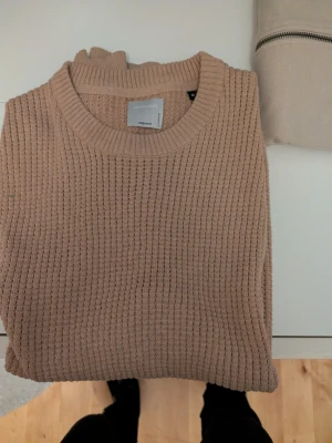 Beige stickad väst från Jack and Jones - Säljer en beige stickad väst från Jack and Jones med rund halsringning och ribbade muddar. Tröjan har en klassisk, rak passform och är gjord i ett mjukt, grovstickat material som passar perfekt till lager-på-lager-stil.