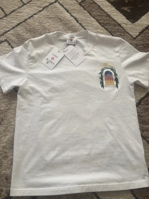 Vit t-shirt från Casablanca - Vit t-shirt från Casablanca med tryck på bröstet som föreställer en byggnad och texten 'Avenida Casablanca'. Klassisk passform och rund hals. Perfekt för dig som gillar stilrena plagg med unika detaljer.