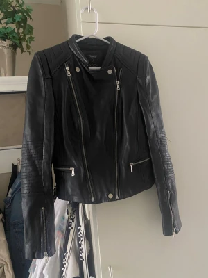 Äkta skinnjacka  från Zara - Snygg svart skinnjacka i äkta skinn från Zara med coola detaljer som silvriga dragkedjor och quiltade partier på axlar och ärmar. Jackan har en asymmetrisk dragkedja framtill och flera fickor med dragkedja. Liten i strl så skulle säga att den passar en S/M