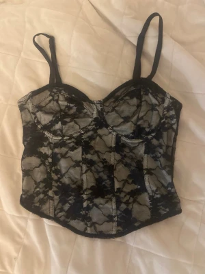 Korsett topp H&M - Snygg korsett topp perfekt till fester. Toppen är beige med svart spets över hela toppen. I storlek xs från H&M divided.
