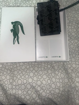Svart Lacoste lanyard plånbok - En snygg och stilig Lacoste plånbok,svår att hitta, nypris 841kr. Hör av er vid minsta lilla😁