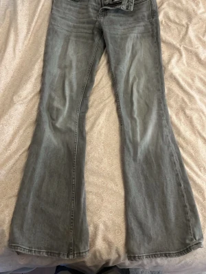 Grå bootcut jeans med utsvängda ben - Säljer ett par grå bootcut jeans med utsvängda ben och klassisk femficksdesign. Jeansen har en snygg tvättad look och normal midja. De sitter väldigt bra på mig men jag har blivit lite för lång. 