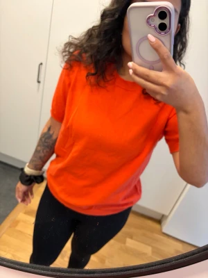Klassisk orange t-shirt i stickat material  - En enkel och stilren orange i mörkare färg t-shirt med rund hals och korta ärmar. T-shirten har en normal passform och är tillverkad i mjukt bomullstyg som känns skönt mot huden. Perfekt till jeans eller tights för en avslappnad look.
