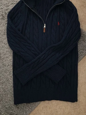 Mörkblå kabelstickad tröja Polo Ralph Lauren - Mörkblå kabelstickad tröja från Polo Ralph Lauren med halv dragkedja. Säljs för jag inte använder den längre. Säljes för 349kr. Kontakta mig om du har frågor.