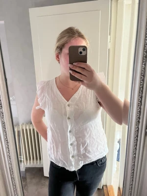 Vit blus med volangärm och knappar - Snygg vit blus med v-ringning och knäppning framtill. Blusen har korta volangärmar och är använd fåtal gånger🩷
