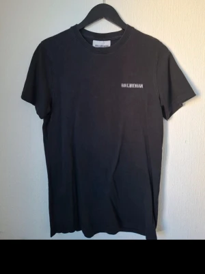 Svart t-shirt från Han Kjøbenhavn - Svart t-shirt från Han Kjøbenhavn med vit broderad logga på bröstet. Klassisk rund hals och korta ärmar. Tillverkad i mjuk bomull för en bekväm känsla och stilren look.