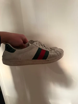 Gucci ace - Säljer ett par klassiska vita sneakers från Gucci med den ikoniska gröna och röda randen på sidan. Skorna är i storlek 42 1/2 och är i bra skick! Hör av er vid frågor!