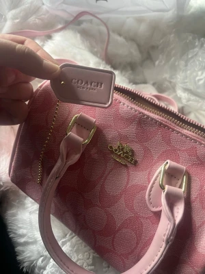 Rosa handväska från Coach - Snygg rosa handväska från Coach med klassiskt monogrammönster och guldfärgade detaljer. 🎀😊 denna har ej kommit till användning så i väldigt bra fint skick! Säljer för lågt pris då jag vill bli av med den! 🥰