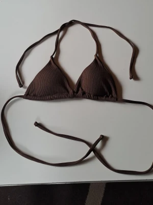 Brun trekantsbikini - Snygg brun trekantsbikini med ribbad struktur och knytband i nacken och ryggen. Perfekt för stranden eller poolen, enkel att justera för bästa passform. Ger en stilren och trendig look till sommaren.