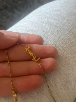YSL armband - Säljer ett elegant armband i guld. Kedjan är tunn och har en snygg platt bricka med varumärkets namn engraverat . Perfekt för dig som vill ha en lyxig och stilren accessoar. Säljer pågrund av att jag redan har en likadan.  Pris kan diskuteras