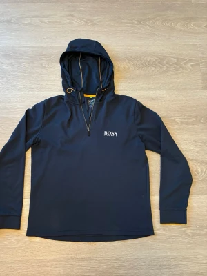 Marinblå/guld hoodie från Hugo Boss - Äkta 🎗️/ kan gå ner i pris 💵/ Snygg marinblå hoodie från Hugo Boss med dragkedja vid halsen och gulddetaljer på snörena. Tröjan har broderad logga på bröstet och är tillverkad i ett strukturerat, mjukt material. Perfekt för en stilren och avslappnad look.