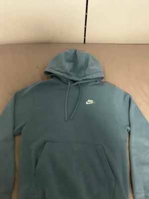 Blå hoodie från Nike med logga - Snygg blå hoodie från Nike med klassisk vit logga på bröstet. Hoodien har huva med dragsko och en stor magficka framtill. Perfekt för en avslappnad och sportig stil. Mjuk och skön bomullsblandning.