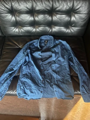 Blå skjorta från H&M - En klassisk blå skjorta från H&M. Skjortan har knappar framtill, lång ärm och en enkel, stilren design som passar till många olika outfits.