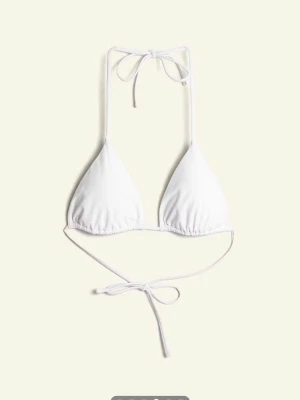 Vit trekantsbikini med knyt - Stilren vit trekantsbikini med tunna band som knyts i nacken och runt ryggen. Klassisk modell som ger en enkel och fräsch look på stranden. Perfekt för dig som gillar minimalistisk stil och vill ha en bikini som alltid känns aktuell. Köptes 2024 och nytvättad 💞