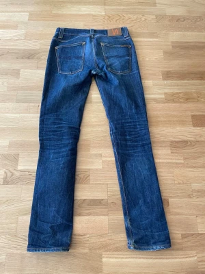 Nudie Jeans i raw denim - Säljer ett par nudie jeans i raw/dry denim! Midja: 41 cm, Ytterben: 105 cm, Benöppning: 16.5 cm. Byxorna är lite slitna vid mellangärdet, men går att sy enkelt! Hör gärna av er vid frågor! 
